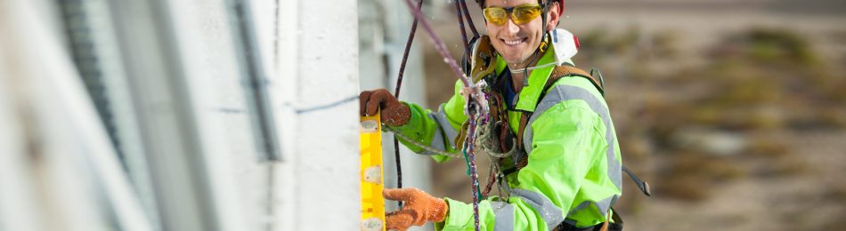 Cheerful industrial climber measuring with level tube during construction works